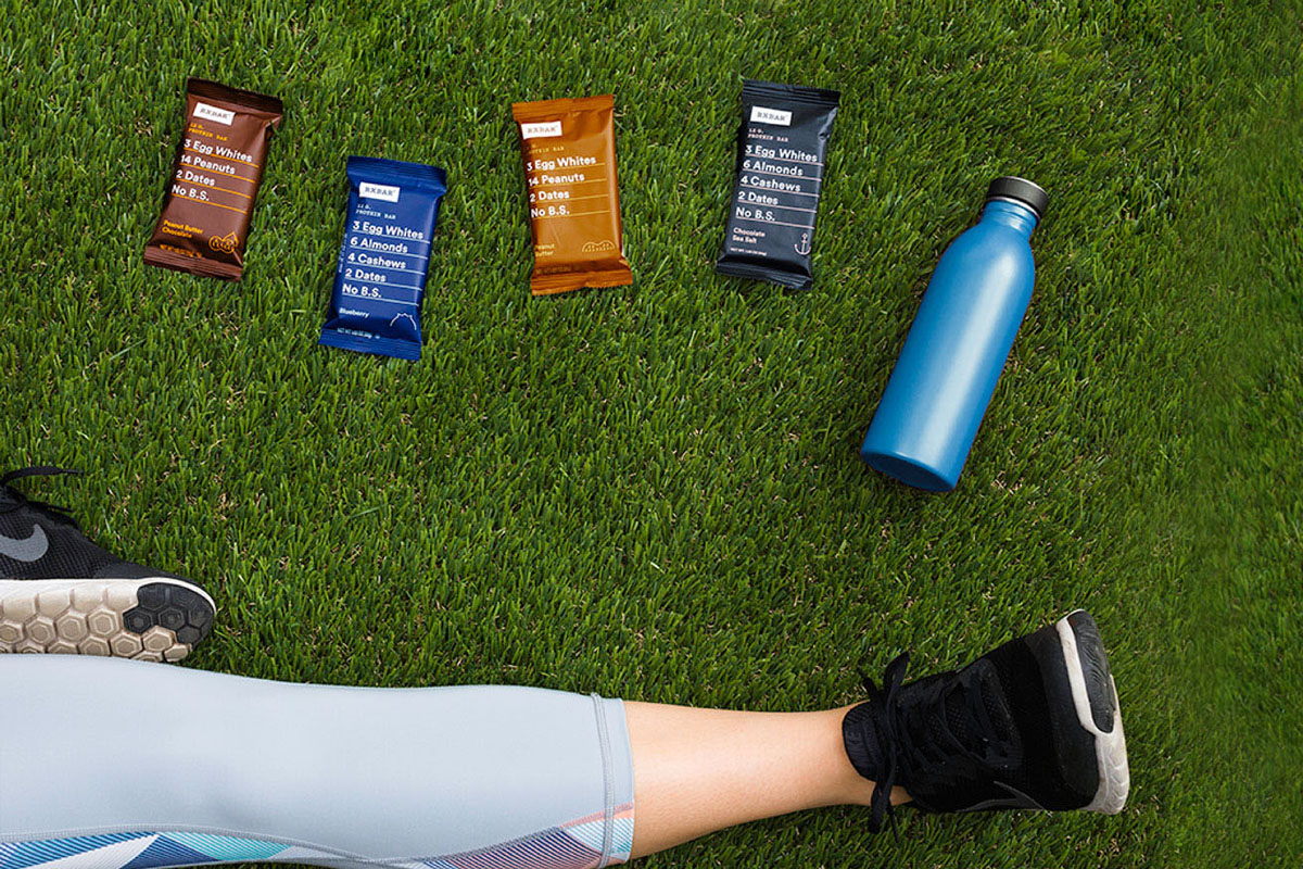 A runner's leg, with a water bottle and RXBARS pictured in the grass