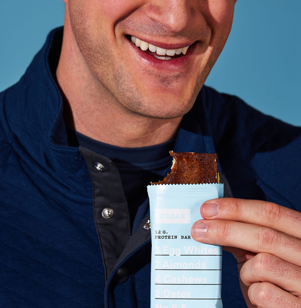 a person smiling, holding an RXBAR