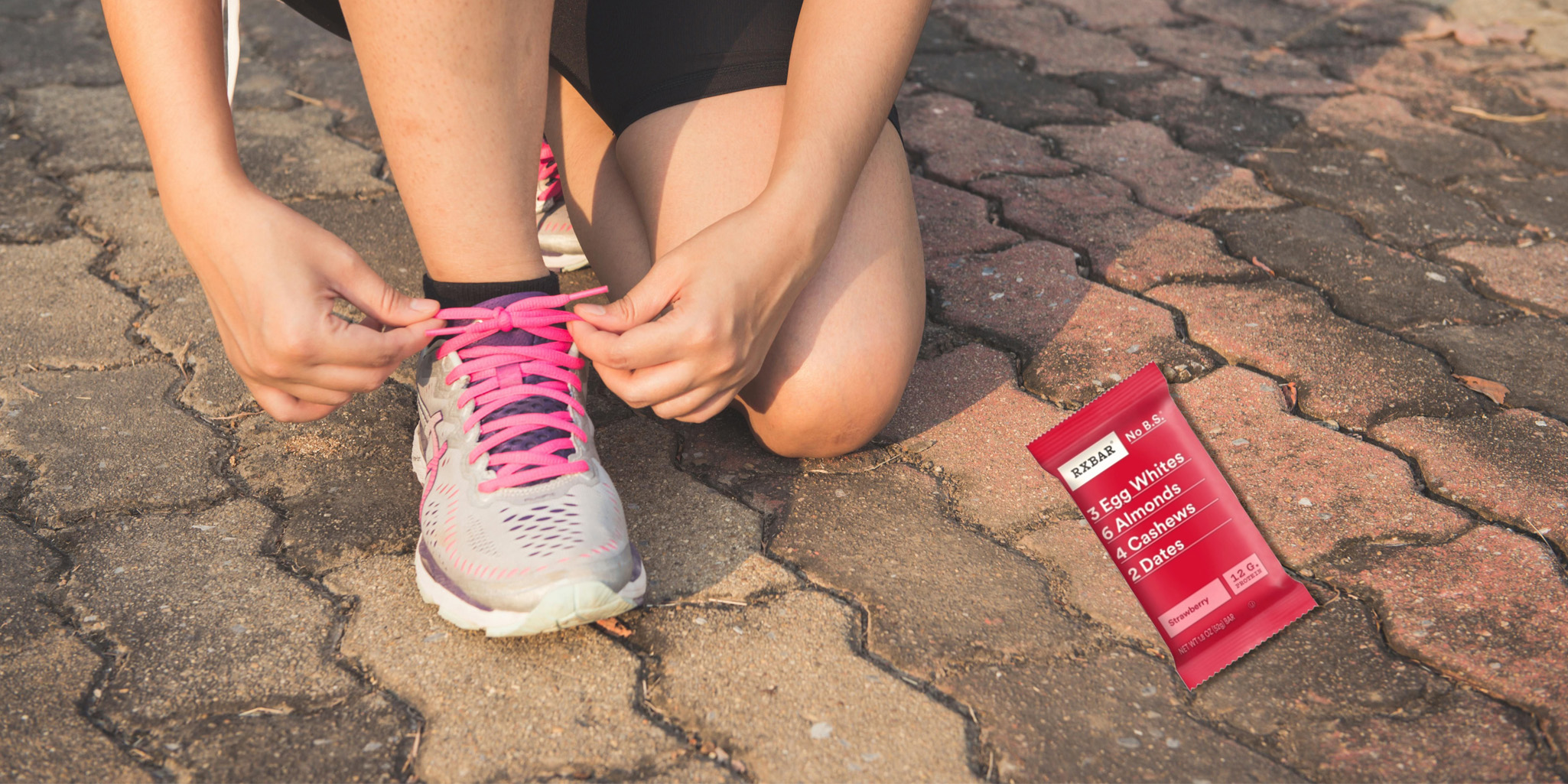 A runner tying their shoe. An RXBAR is on the ground.