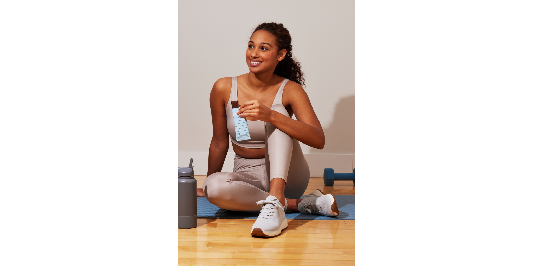 Smiling woman sitting on yoga mat while eating an rxbar and looking off into the distance