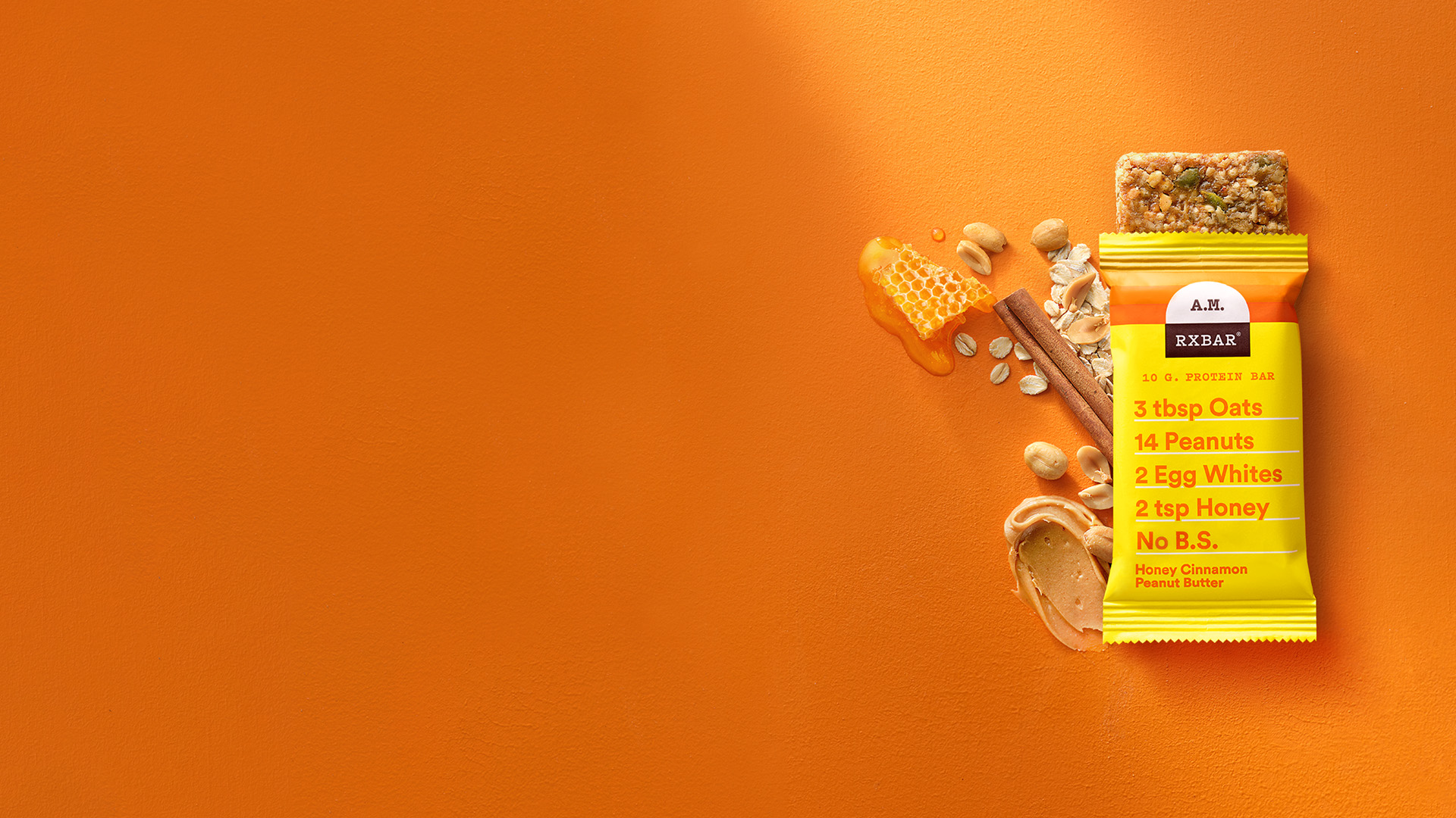 A Honey Cinnamon Peanut Butter A.M. RXBAR on an orange background with honey, cinnamon, oats and peanut butter